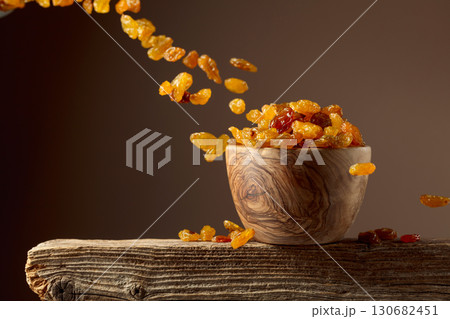 Yellow sultana raisins pour into a wooden bowl. 130682451