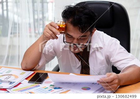 Stressed businessman in office holding whiskey glass while reading financial documents, symbolizing overwork, pressure, unhealthy lifestyle, alcohol addiction, financial stress, and burnout Stressed businessman in office holding whiskey glass while reading financial documents, symbolizing overwork, pressure, unhealthy lifestyle, alcohol addiction, financial stress, and burnout 130682499