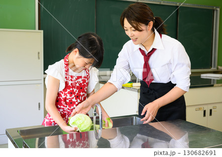 料理教室で調理を学ぶ小学生の女の子と料理の先生　教育と食育イメージ 130682691