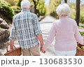 An elderly couple walks hand-in-hand down a peaceful park path on a sunny day, each carrying a wicker basket. A serene and intimate moment of companionship An elderly couple walks hand-in-hand down a peaceful park path on a sunny day, each carrying a wicker basket. A serene and intimate moment of companionship 130683530