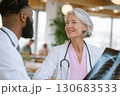 elderly female doctor holding x-ray image and smiling while talking to colleague in modern medical office elderly female doctor holding x-ray image and smiling while talking to colleague in modern medical office 130683533