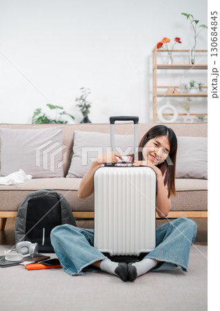 Smiling woman sitting with suitcase in cozy living room, preparing for a travel journey. Modern lifestyle and adventure concept. Smiling woman sitting with suitcase in cozy living room, preparing for a travel journey. Modern lifestyle and adventure concept. 130684845