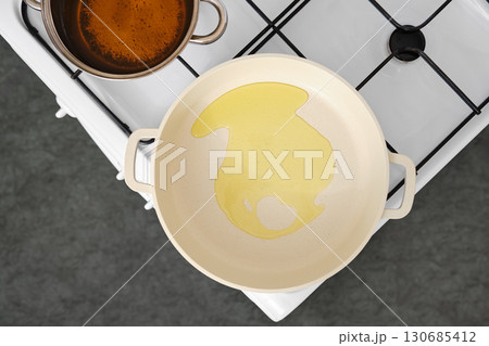 Cooking oil is poured into a frying pan on a stovetop for meal preparation Cooking oil is poured into a frying pan on a stovetop for meal preparation 130685412