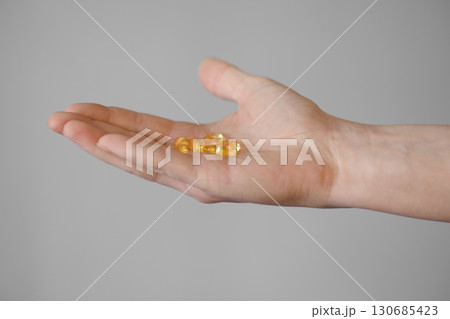Hand holding several yellow capsules on a neutral background in indoor lighting 130685423