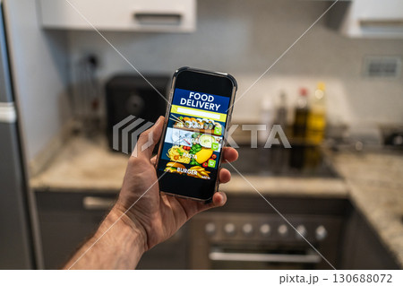 Hand holding smartphone with food delivery app interface on screen, showing sushi, vegan, pasta and burger categories. Hand holding smartphone with food delivery app interface on screen, showing sushi, vegan, pasta and burger categories. 130688072