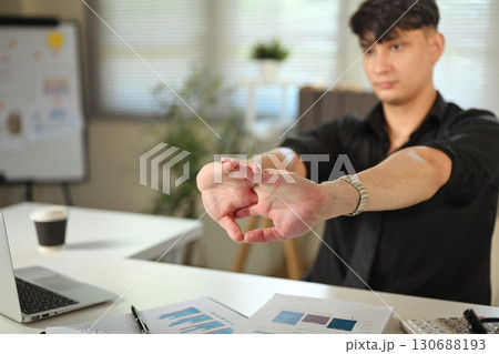 Businessman stretching hands at office desk to relieve stress and improve focus during workday Businessman stretching hands at office desk to relieve stress and improve focus during workday 130688193