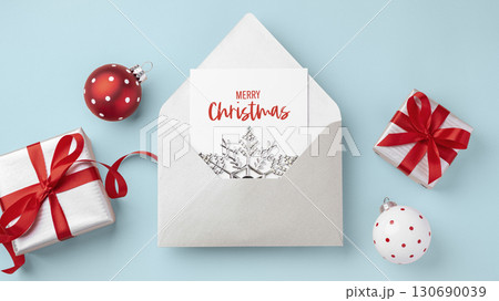 Merry Christmas holiday card in envelope and present gift boxes with red bow ribbon and xmas ball ornament on light blue background Merry Christmas holiday card in envelope and present gift boxes with red bow ribbon and xmas ball ornament on light blue background 130690039