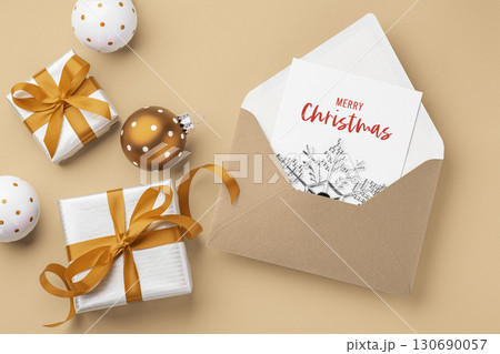 Christmas holiday card in envelope with present gift boxes with gold bow ribbon and xmas ball ornament on brown background Christmas holiday card in envelope with present gift boxes with gold bow ribbon and xmas ball ornament on brown background 130690057