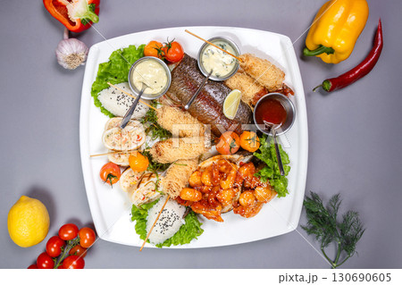 Grilled fish, spicy shrimp, spring rolls, and rice on a white plate. Top view on gray background Grilled fish, spicy shrimp, spring rolls, and rice on a white plate. Top view on gray background 130690605