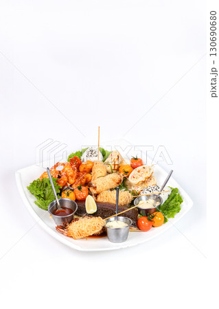 Grilled fish, spicy shrimp, spring rolls, rice balls, and sauces on a white plate. 130690680