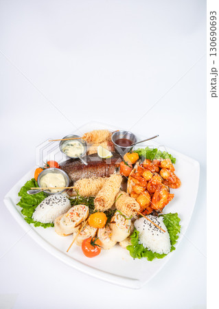 Grilled fish, spicy shrimp, spring rolls, rice balls, and sauces on a white plate. Grilled fish, spicy shrimp, spring rolls, rice balls, and sauces on a white plate. 130690693