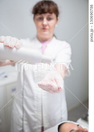 Beautician in gloves pouring cosmetic liquid from bottle for skincare treatment in salon Beautician in gloves pouring cosmetic liquid from bottle for skincare treatment in salon 130690786