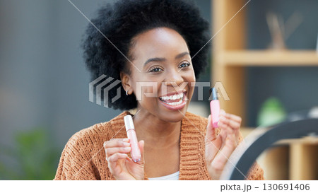 Woman influencer recording a makeup tutorial for her beauty channel, blog or live streaming at home. Young African female content creator filming a video with cosmetic products in the living room. Woman influencer recording a makeup tutorial for her beauty channel, blog or live streaming at home. Young African female content creator filming a video with cosmetic products in the living room. 130691406