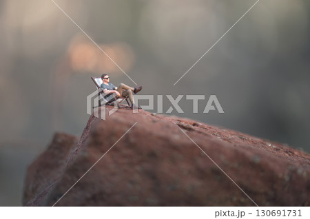 Miniature man relaxing on top of a mountain 130691731
