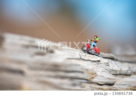 Miniature figurine of a man riding a moped on a tree trunk Miniature figurine of a man riding a moped on a tree trunk 130691736