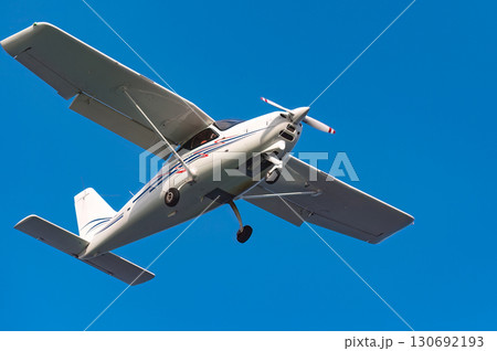 Compact aircraft gliding across brilliant azure sky, embodying aerial freedom with sunlight gleaming on wings Compact aircraft gliding across brilliant azure sky, embodying aerial freedom with sunlight gleaming on wings 130692193