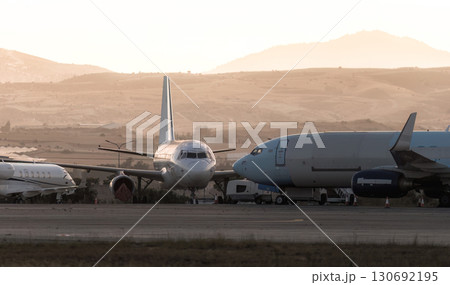 Parked airplanes sitting on the tarmac of an airport at sunset with hills in the background. Larnaca, Cyprus Parked airplanes sitting on the tarmac of an airport at sunset with hills in the background. Larnaca, Cyprus 130692195