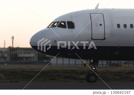 Commercial jet rolling along tarmac, sunset glowing behind sleek aircraft, highlighting runway before takeoff Commercial jet rolling along tarmac, sunset glowing behind sleek aircraft, highlighting runway before takeoff 130692197