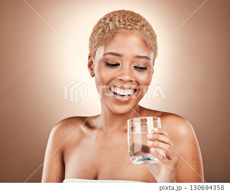 Black woman, drinking water and glass for health on a brown background for skincare or diet. Aesthetic model person smile for clean and sustainable liquid for healthy lifestyle and wellness in studio 130694358