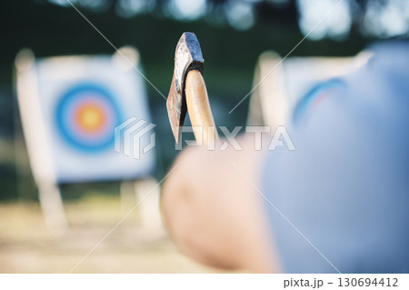 Man throwing axe at sports range, archery training or practice with board circle for goal, game and exercise. Strong person closeup with weapon for tomahawk competition, gaming park and eye target 130694412
