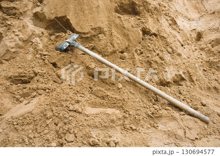 Construction sand pile with iron shovel, beside paved road Construction sand pile with iron shovel, beside paved road 130694577