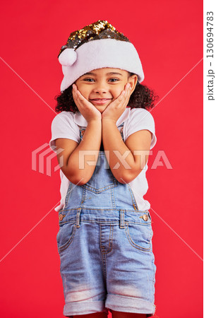 Little girl, face and portrait smile for Christmas, celebration or surprise isolated on a red studio background. Happy child smiling in happiness with hands looking adorable for festive season gift 130694783