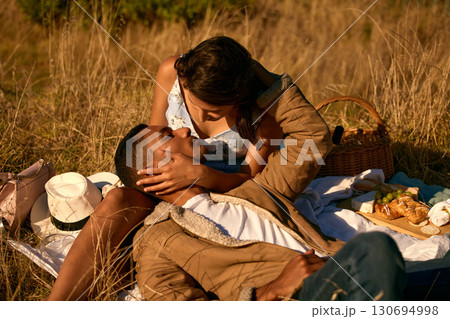 Love, sunset and picnic with couple in field for summer break, relax and romantic date. Happy, kiss and food with man and woman affectionate in grass of countryside for travel, bonding and peace Love, sunset and picnic with couple in field for summer break, relax and romantic date. Happy, kiss and food with man and woman affectionate in grass of countryside for travel, bonding and peace 130694998