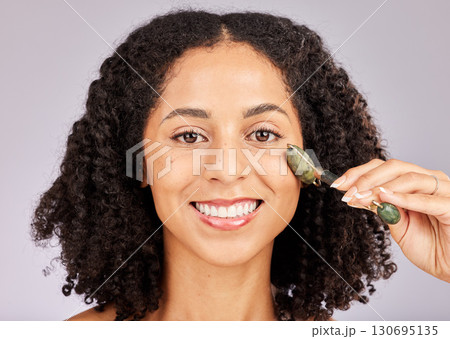 Jade facial roller, portrait and face skin glow of a black woman with beauty stone tool in studio. Wellness, dermatology and young model with spa, skincare and happiness from cosmetics treatment 130695135