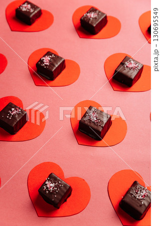 Dark chocolate candy on red paper hearts, flat lay on pink background, Valentine concept 130695549