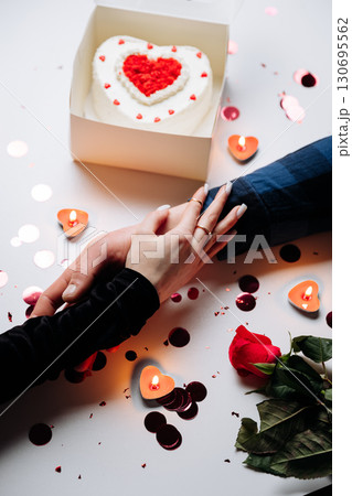 Romantic Valentine's Day moment with cake, candles, and a couple holding hands 130695562