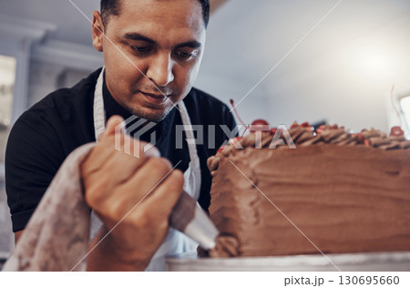 Piping, kitchen and man baking a cake with chocolate or pastry chef preparing a recipe at a bakery. Food, dessert and professional baker making a sweet meal and adds cream or icing Piping, kitchen and man baking a cake with chocolate or pastry chef preparing a recipe at a bakery. Food, dessert and professional baker making a sweet meal and adds cream or icing 130695660