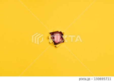 Close-up of human showing tongue through torn yellow paper 130695711