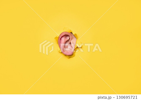 Close-up of human ear through torn yellow paper Close-up of human ear through torn yellow paper 130695721
