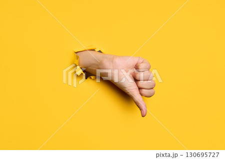 Thumb down sign gesture through hole in torn yellow paper background Thumb down sign gesture through hole in torn yellow paper background 130695727