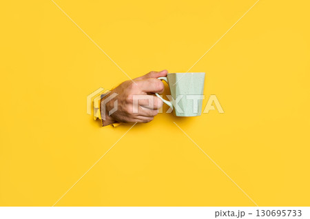 Female hand holding cup on yellow background Female hand holding cup on yellow background 130695733