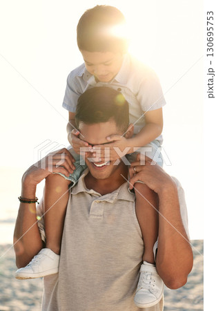 Beach, travel and child on shoulder of father with hands cover eyes for surprise game, quality time and playing. Family, love and happy boy with dad by ocean bond on adventure, holiday and vacation 130695753