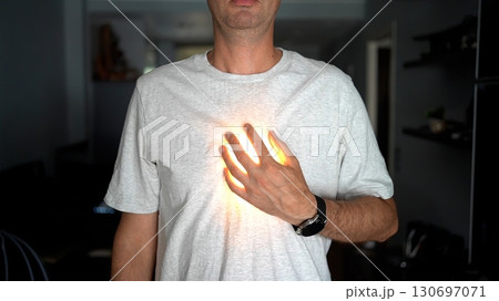 A man in a white t-shirt places his hand on his chest with a glowing light effect under his hand, symbolizing heart, energy, or inner power. 130697071