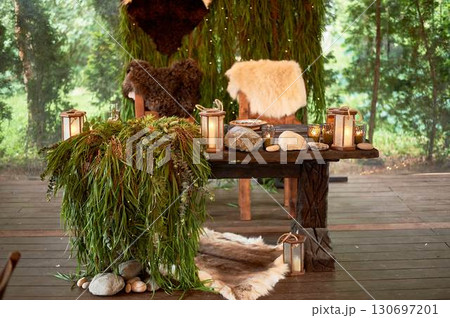 Two thrones for the wedding couple, in the Viking style. Heavy wooden tables and chairs decorated with animal skins and greenery. Massive composition 130697201