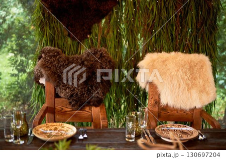 Two thrones for the wedding couple, in the Viking style. Heavy wooden tables and chairs decorated with animal skins and greenery. Massive composition 130697204