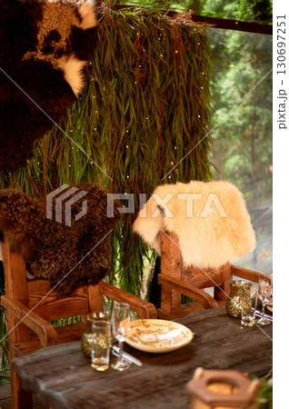 Two thrones for the wedding couple, in the Viking style. Heavy wooden tables and chairs decorated with animal skins and greenery. Massive composition 130697251