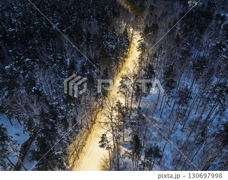 Aerial view of illuminated road in night winter forest with high pine or spruce trees covered by snow. Aerial view of illuminated road in night winter forest with high pine or spruce trees covered by snow. 130697998