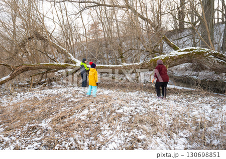 Families gather in winter to clear fallen tree from snowy creek in serene park, creating a safe space for outdoor play and exploration amidst nature Families gather in winter to clear fallen tree from snowy creek in serene park, creating a safe space for outdoor play and exploration amidst nature 130698851