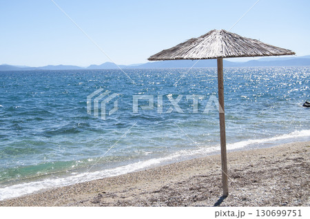 An umbrella on the empty beach. A seashore background with an umbrella. A seascape frame with copy space. Travelling and tourism background. 130699751