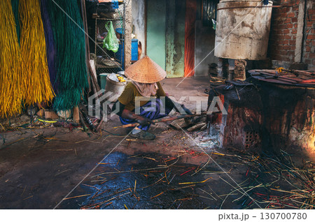 Vietnamese woman wearing a traditional straw hat works in a cane dyeing workshop at a woven mat factory in Vietnam. A woman does dirty hard men's work 130700780