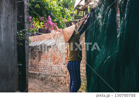Vietnamese woman in straw hat dries dyed green reeds at a woven mat factory in a village in Vietnam Vietnamese woman in straw hat dries dyed green reeds at a woven mat factory in a village in Vietnam 130700788
