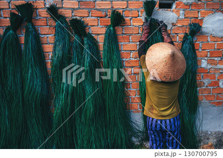 Vietnamese woman in straw hat dries dyed green reeds at a woven mat factory in a village in Vietnam Vietnamese woman in straw hat dries dyed green reeds at a woven mat factory in a village in Vietnam 130700795