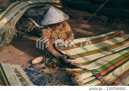 Vietnamese woman worker in traditional straw hat Non La works at a reed woven mat factory in craft village in Vietnam Vietnamese woman worker in traditional straw hat Non La works at a reed woven mat factory in craft village in Vietnam 130700802