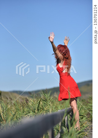 Woman with red hair in red dress walking through scenic natural wetland pathway 130701214