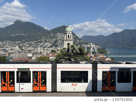 スイスのルガーノ駅から見たルガーノの大聖堂と手前はイタリア国境方面までを結ぶ鉄道のFLP 130702802