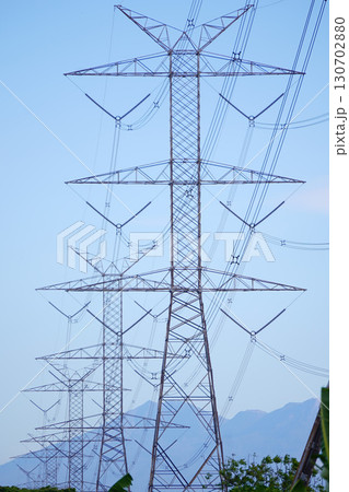 High-voltage power lines and transmission towers against a clear blue sky, illustrating electrical infrastructure and energy transport. 130702880